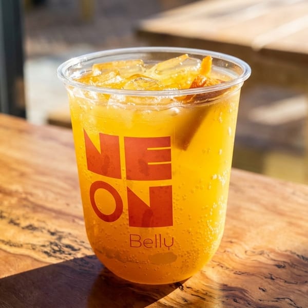 A Neon Belly branded cup filled with a sparkling orange drink and ice sits on a wooden table.