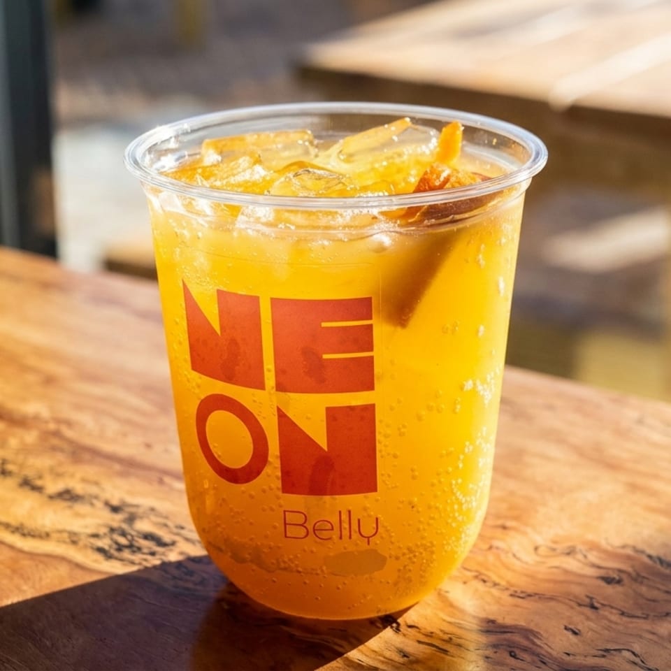 A Neon Belly branded cup filled with a sparkling orange drink and ice sits on a wooden table.