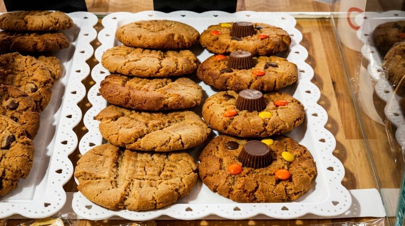 Rows of peanut butter cookies and cookies with Reese's cups on white scalloped trays.