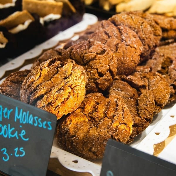 Sugar-dusted ginger molasses cookies on a white tray with a price tag in a bakery display.