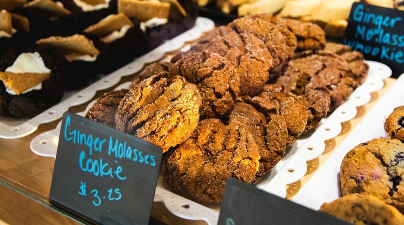 Close-up of ginger molasses cookies on a white tray with a price tag in a bakery display.